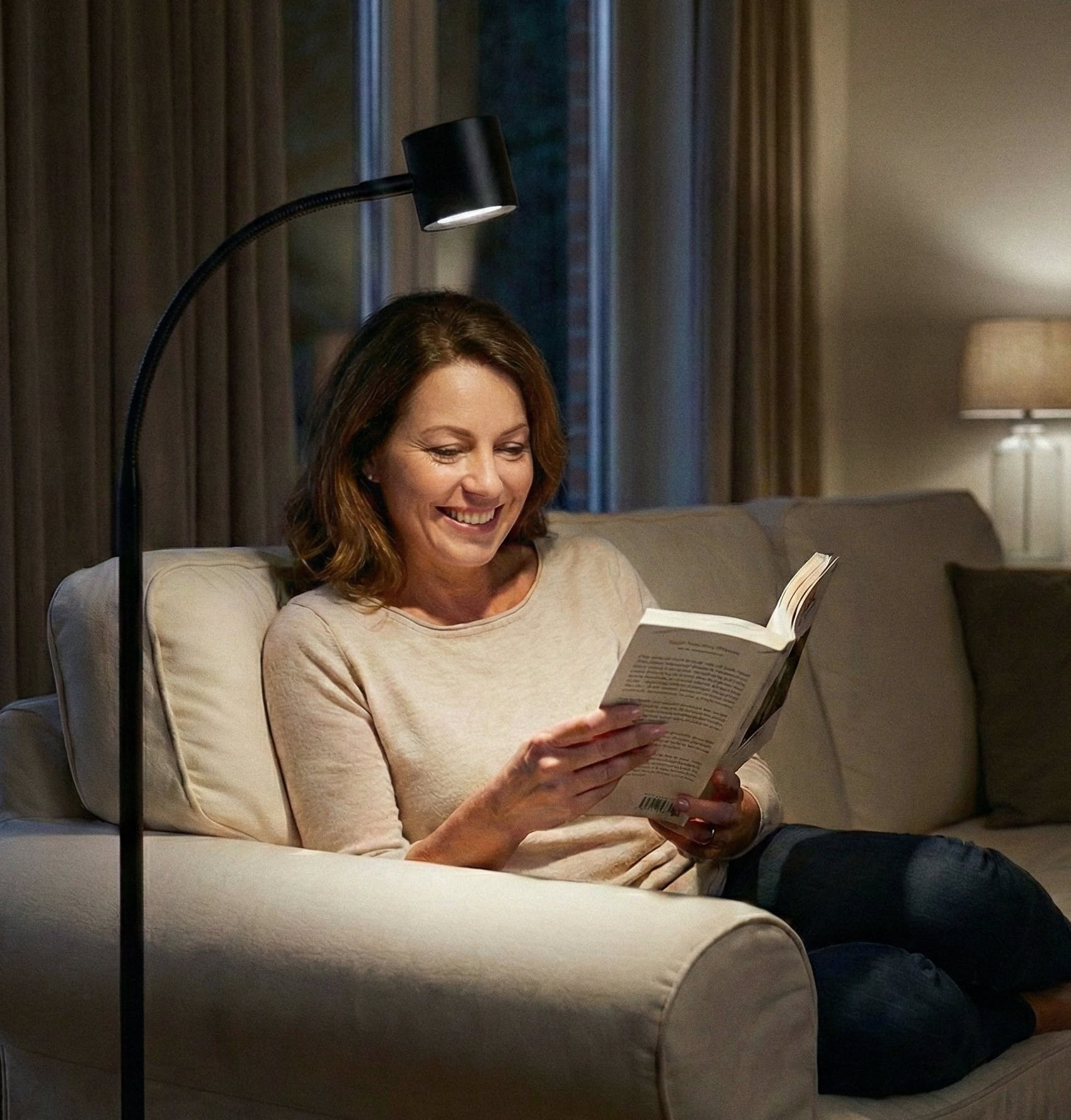 Woman reading a book in a cosy living room with a the Clairty reading light illuminating her.