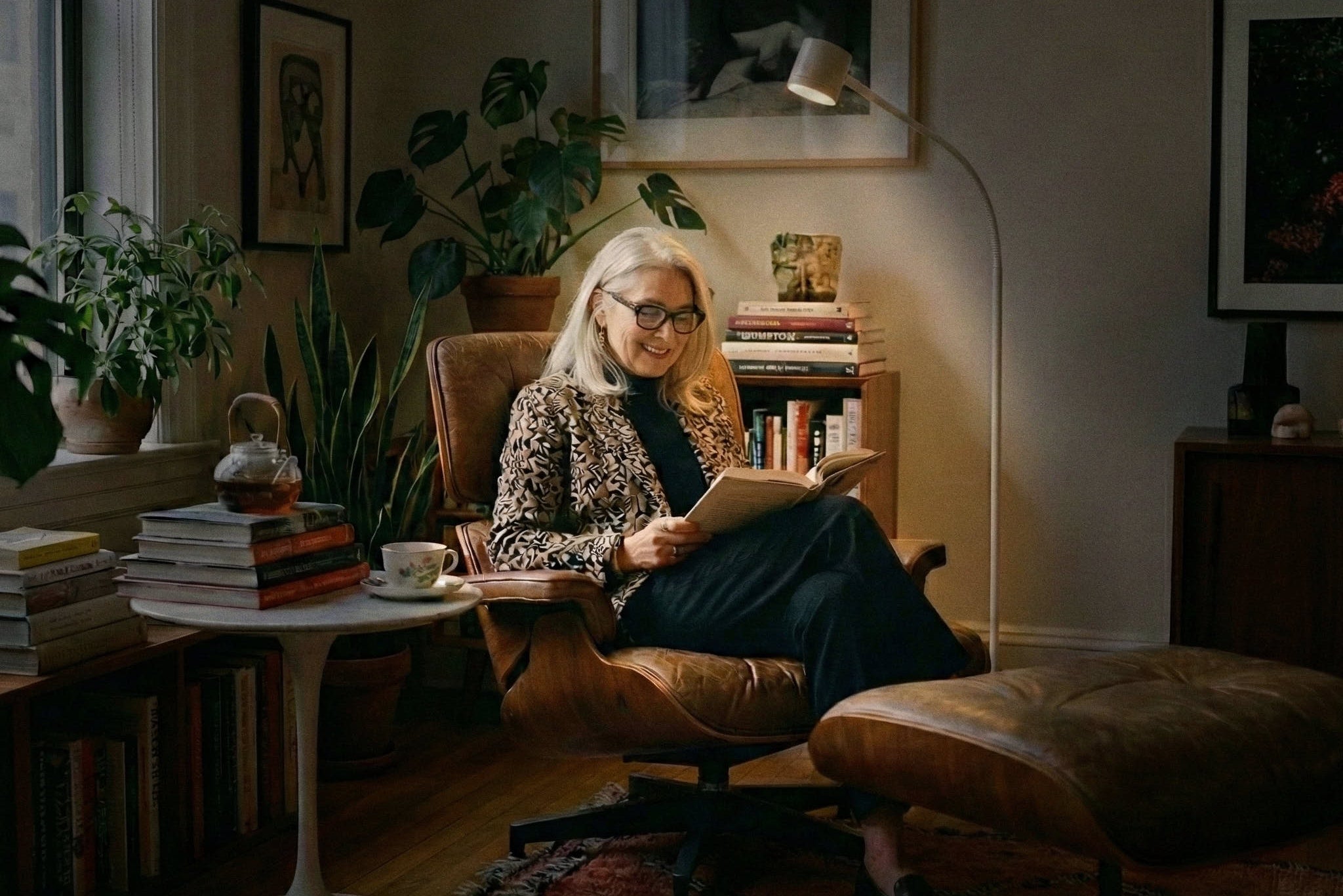 Woman reading a book in a cozy living room with plants and books around using the Clarity task light