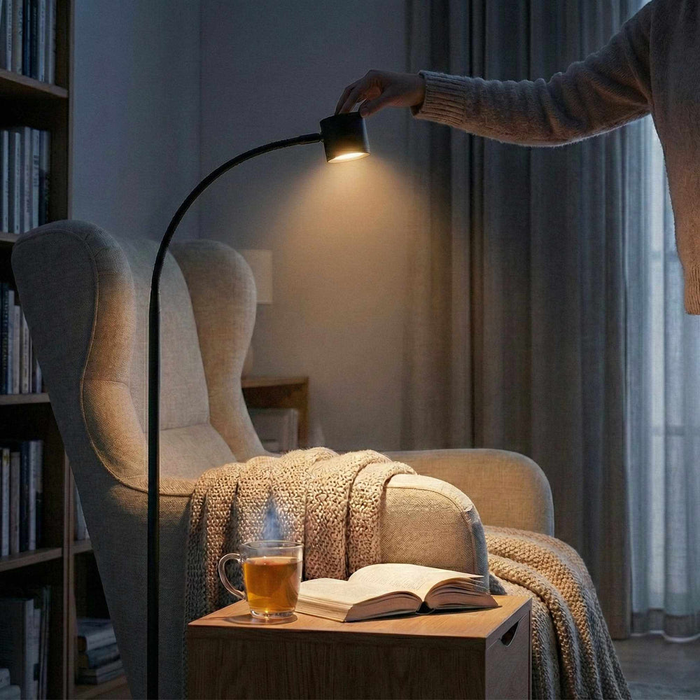 Person adjusting the Clarity floor lamp in a cosy living room with a book and mug on a table.